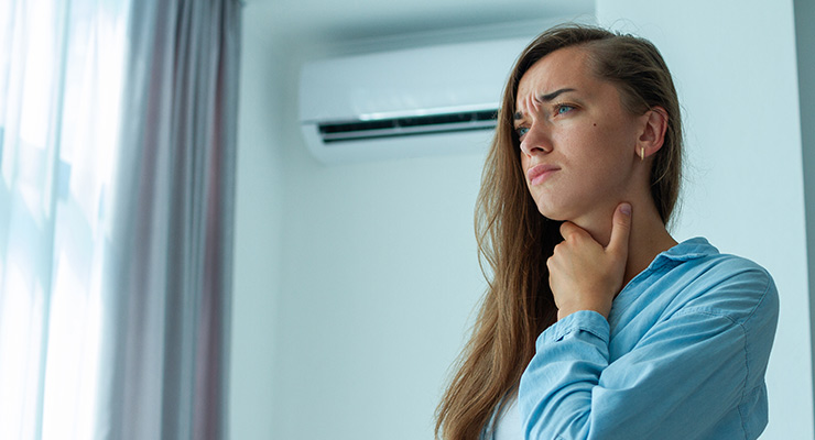 woman feeling throat with air conditioner in background
