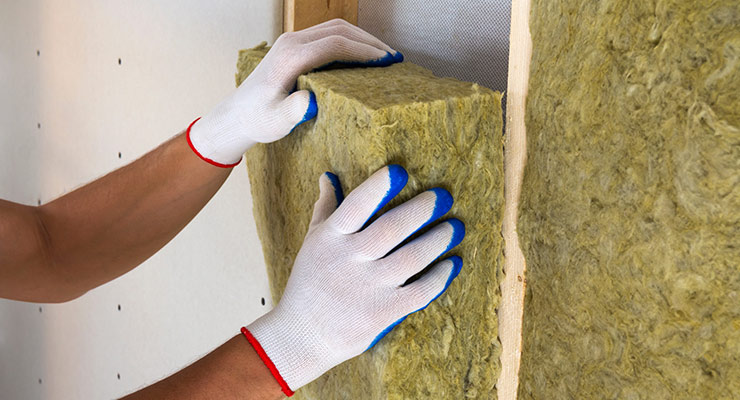 pair of hands inserting insulation into wall